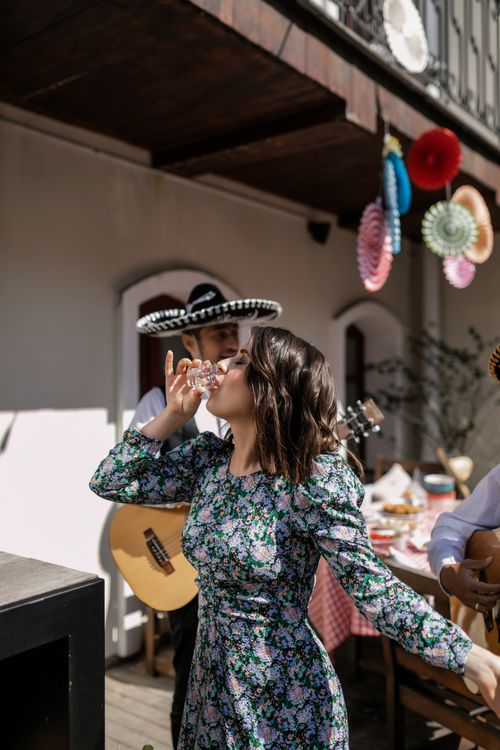 Free A woman in a floral dress drinks at an outdoor fiesta with live mariachi music. Stock Photo