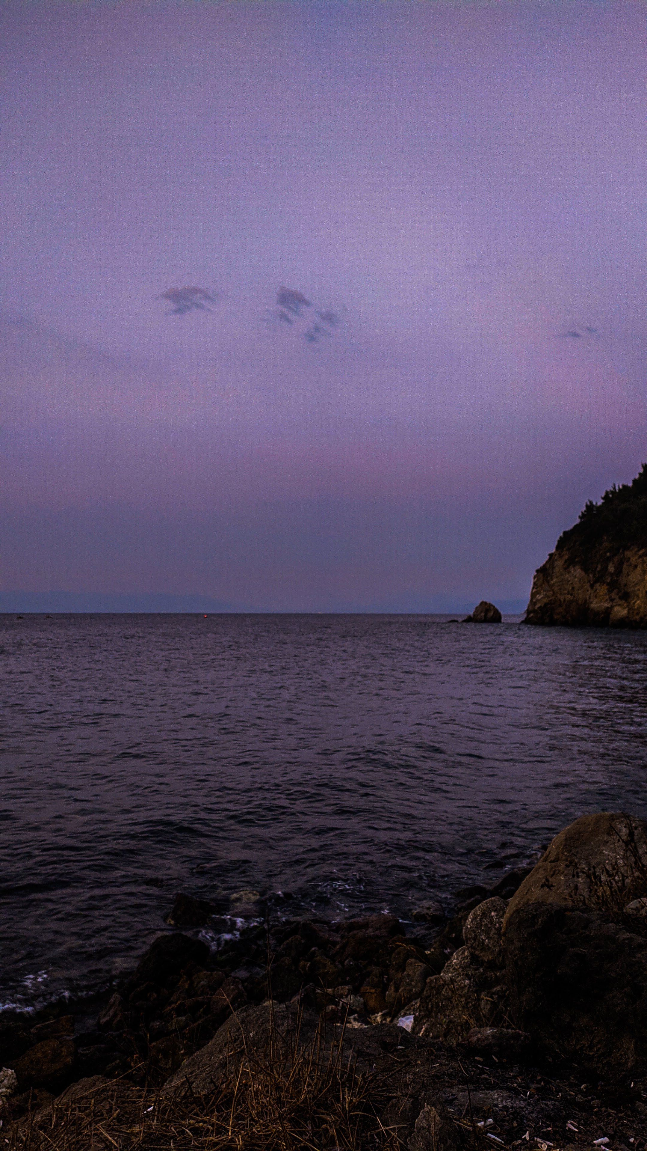 Capture the calming twilight over a rocky coastline, with muted colors reflecting on the sea.