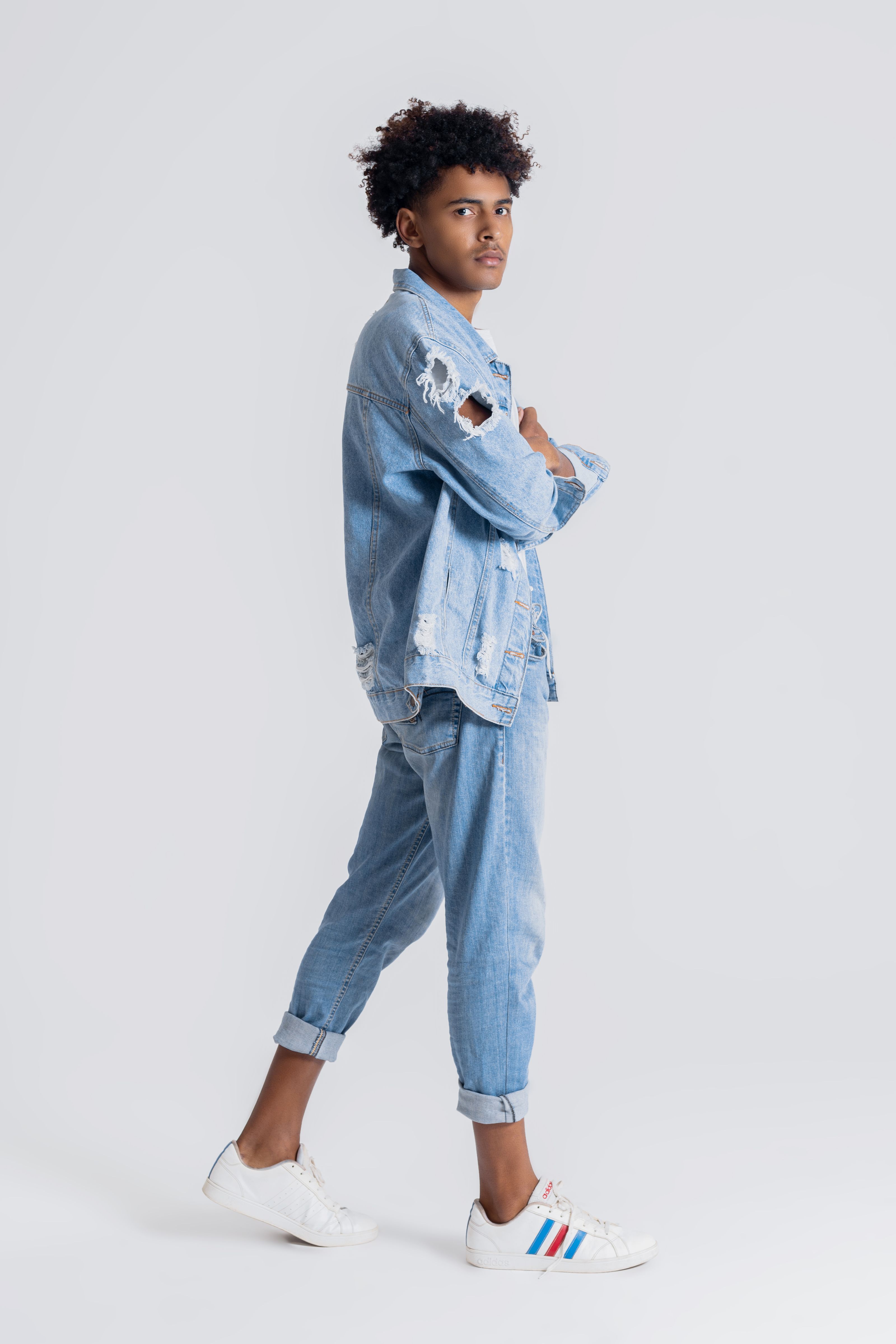 Modelo adolescente estiloso em denim rasgado posando confiantemente contra um fundo branco.