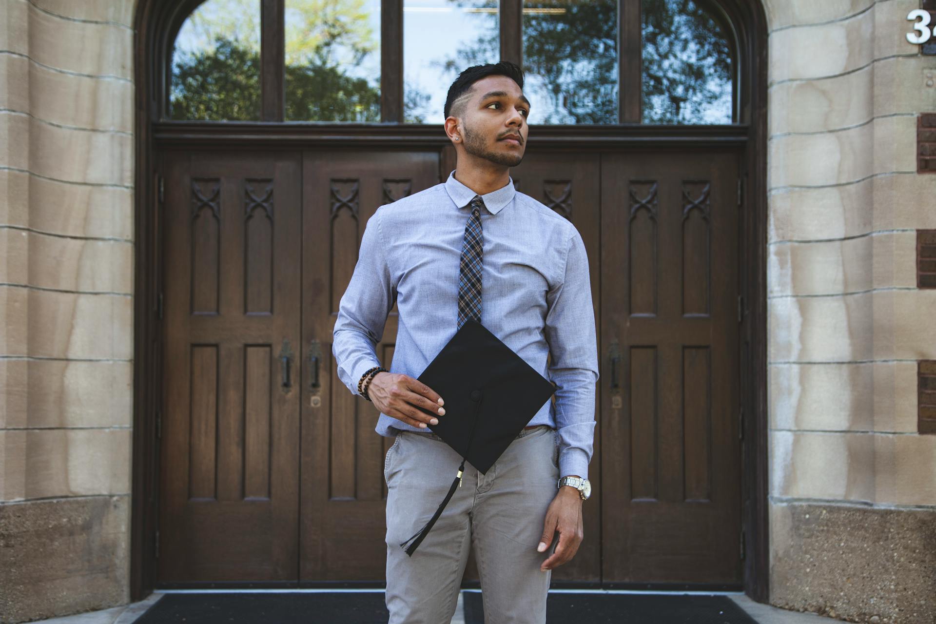 Man in Formal Attire Holding a Graduation Cap while Looking Afar