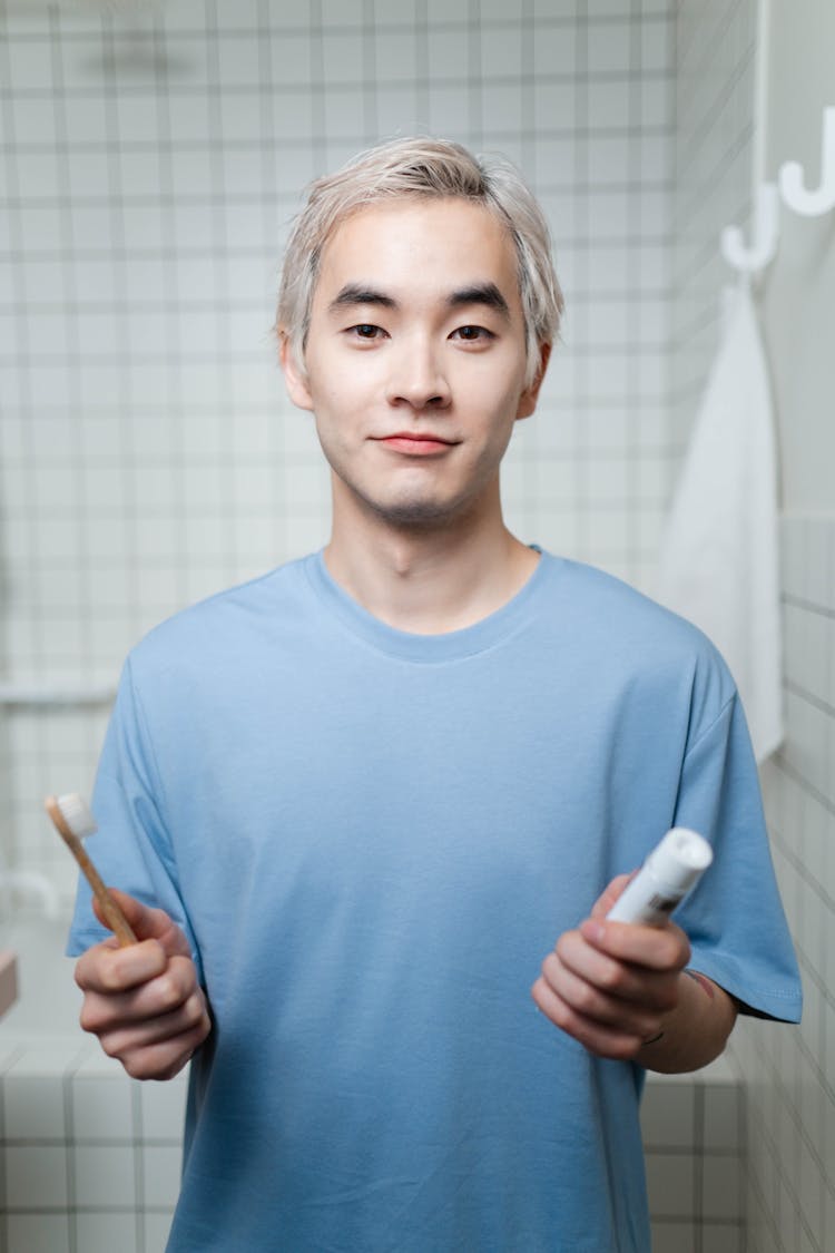 Man In Blue Crew Neck Shirt Holding A Toothbrush And Toothpaste