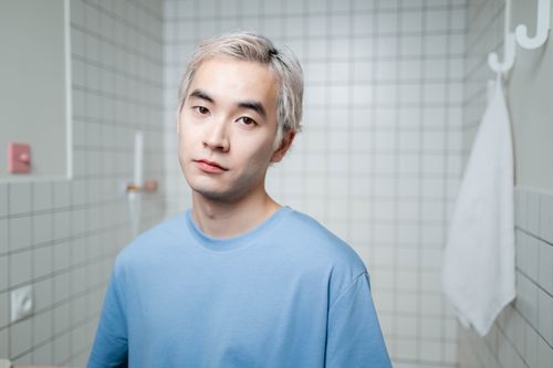 Free Portrait of a young man with blonde hair in a contemporary bathroom setting, exhibiting confidence. Stock Photo