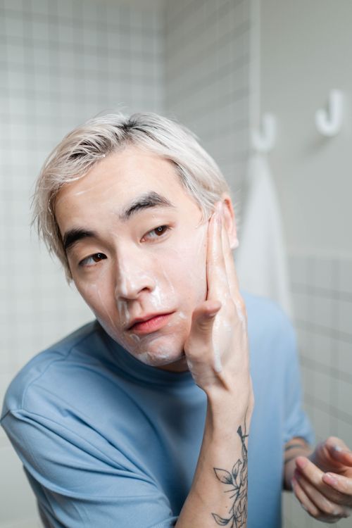 Free Asian man applying foaming cleanser for healthy skin care routine indoors. Stock Photo