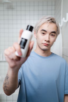 Young Asian man in bathroom showcasing a skincare product, emphasizing fresh skincare routine.