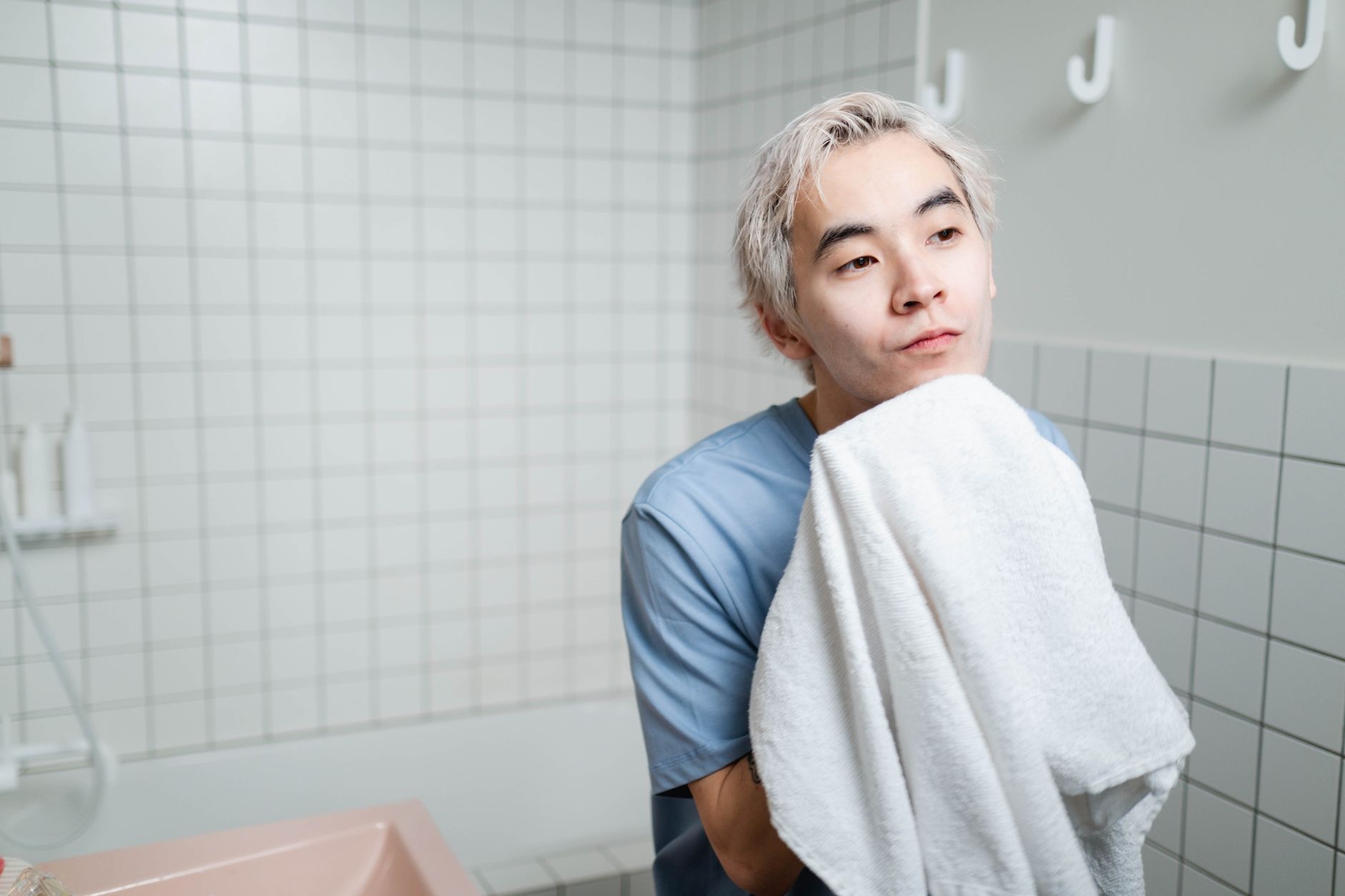 Young man gently drying face with towel in a modern tiled bathroom setting.