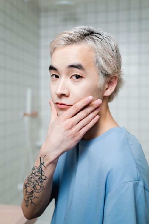 Free A young adult man in a bathroom applying skincare, emphasizing hygiene and self-care. Stock Photo