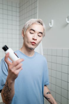 Portrait of a young man holding a skincare product in a contemporary bathroom setting.