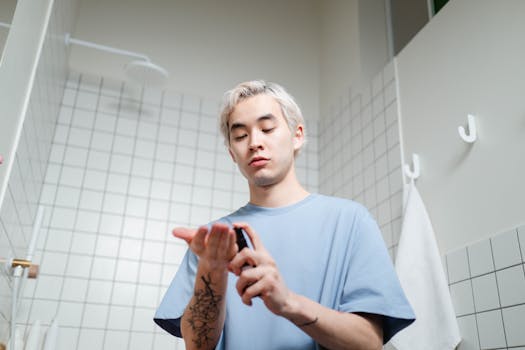 Young man applying skincare serum in a modern bathroom setting.