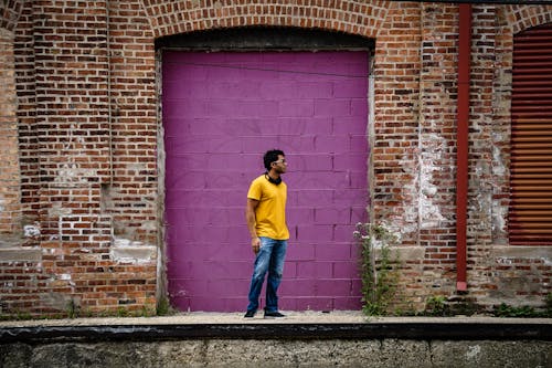 Free Woman in Yellow Long Sleeve Shirt and Blue Denim Jeans Standing Beside Brick Wall Stock Photo