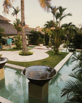Serene tropical resort landscape in Bali with palm trees, lush gardens, and tranquil water features.