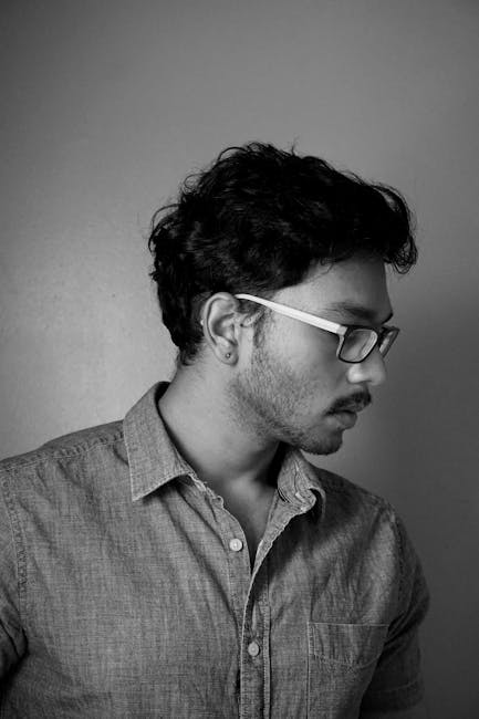 A serious black and white portrait of a man with glasses in side view.