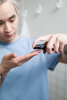 A young man in a bathroom applying skincare serum to his hands.