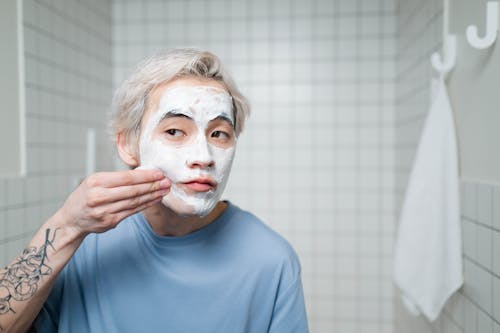 Man in Blue Crew Neck Shirt Applying Cream On His Face