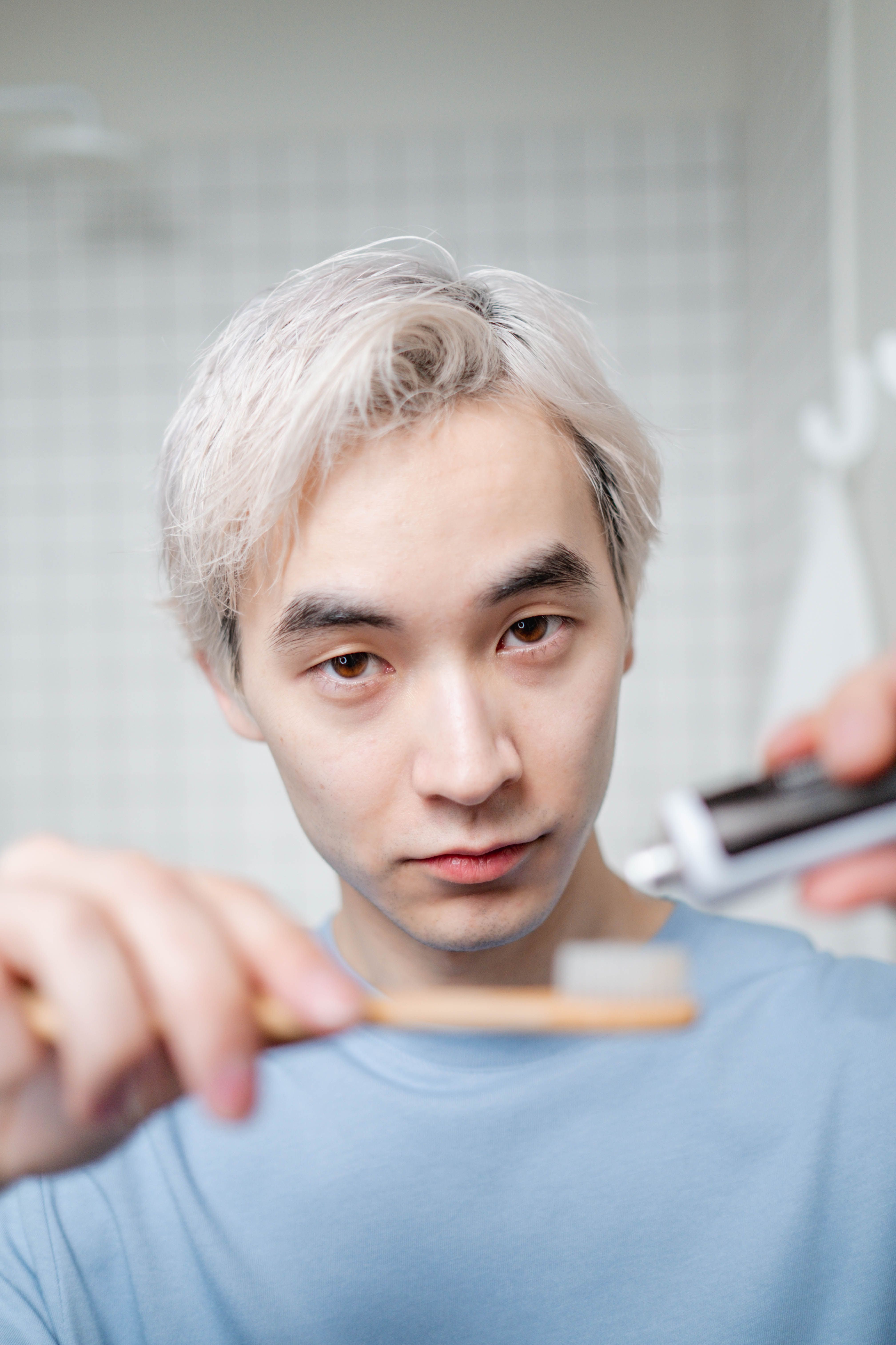 Asian man applying toothpaste to toothbrush for morning routine in bathroom.