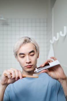 Young Asian man applying toothpaste to a brush during his morning oral hygiene routine.