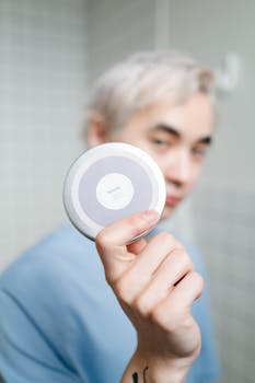 Asian man indoors holding a facial skincare product, emphasizing self-care and beauty routine.
