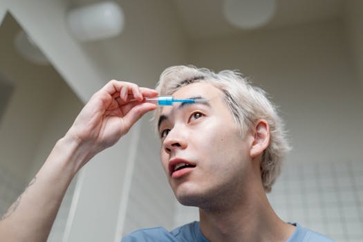 A young man applying eyebrow gel in a contemporary bathroom setting, focusing on self-care.
