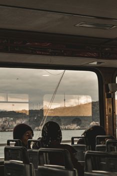 Travelers sit on a bus with a scenic coastal town view, observed through large windows.