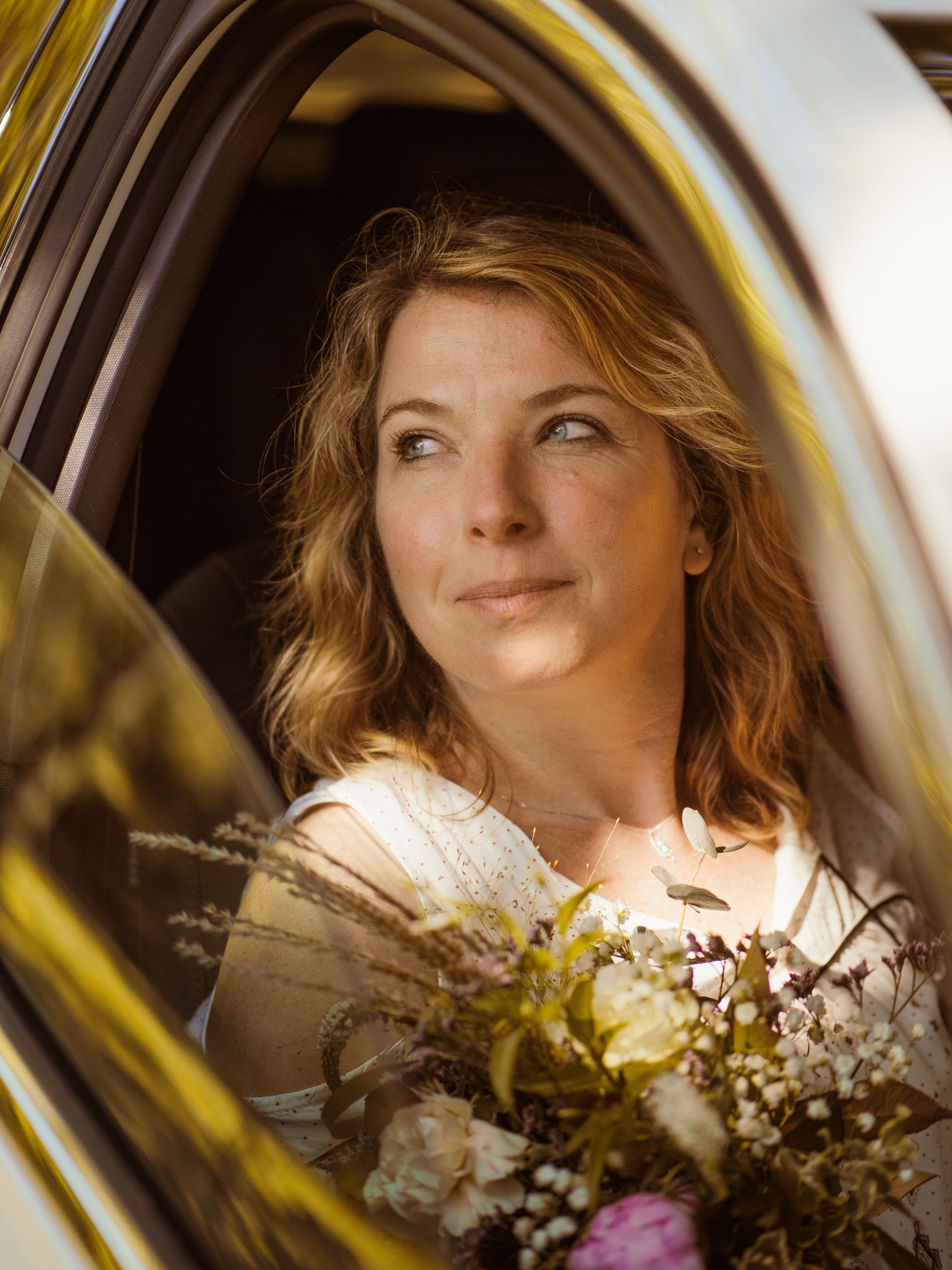 Beautiful woman with a bouquet, gazing out of a car window in France. Bright and serene atmosphere.