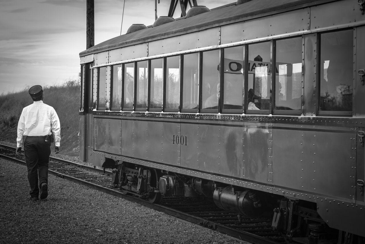 black and white image of a conductor walking towards a vintage train i