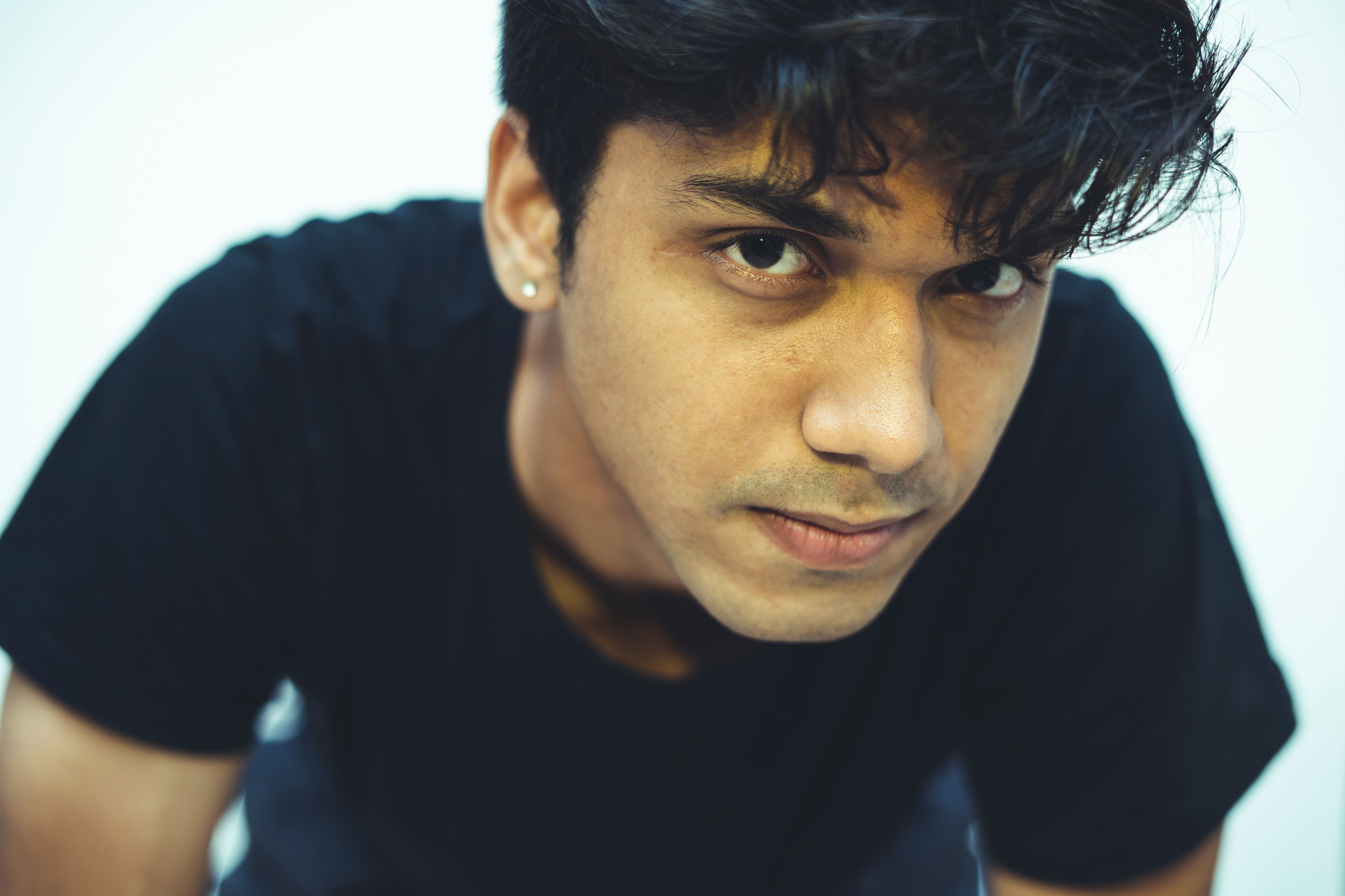 A close-up portrait of a young man wearing a black shirt, looking intently at the camera.
