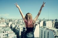 一名妇女站在屋顶上，双手比出和平手势，俯瞰城市景观