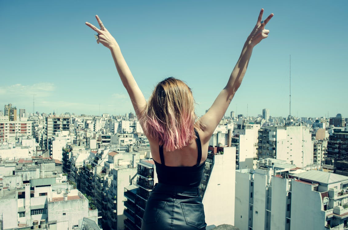 Free Woman Standing on Rooftop Putting Hands in the Air Under Clear Sky Stock Photo