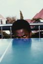 Frowning African American male player looking above table for tennis and looking at camera with attention