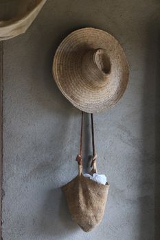 A straw hat and woven bag hanging on a simple wall, showcasing rustic decor style.