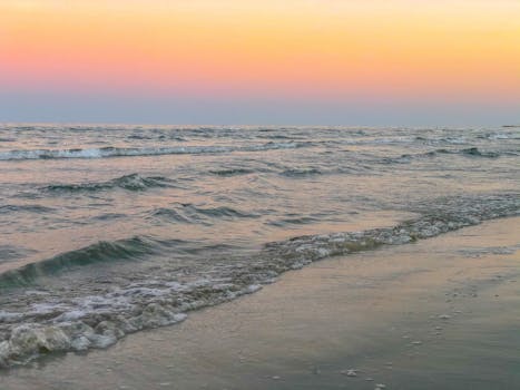 A tranquil beach scene at sunset with soft waves and colorful sky.