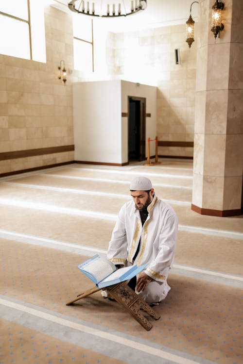 A Man in White Robe Reading the Koran