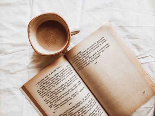 Free A top view of a coffee cup and an open book on a white sheet, creating a cozy and relaxed atmosphere. Stock Photo