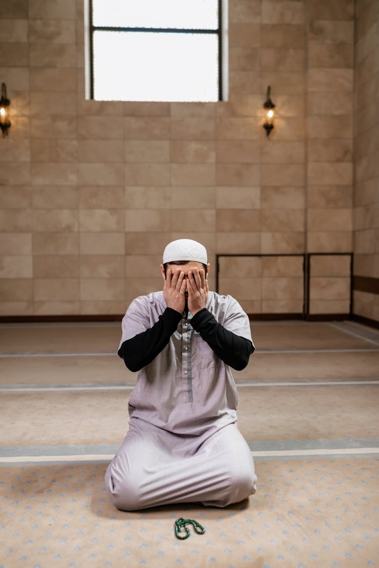 A Man Kneeling On The Floor While Covering His Face