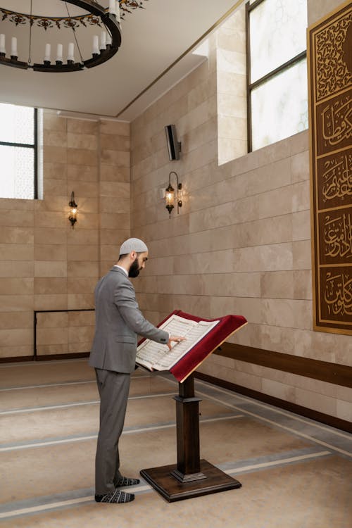 Man in Gray Suit Standing while Reading a Book