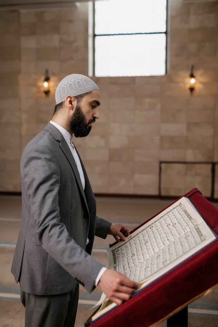 A Bearded Man In Gray Suit Reading A Quran