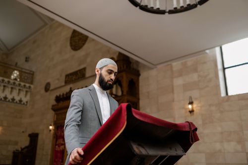 Free A man in traditional attire stands by a lectern in a mosque, engaged in prayer. Stock Photo