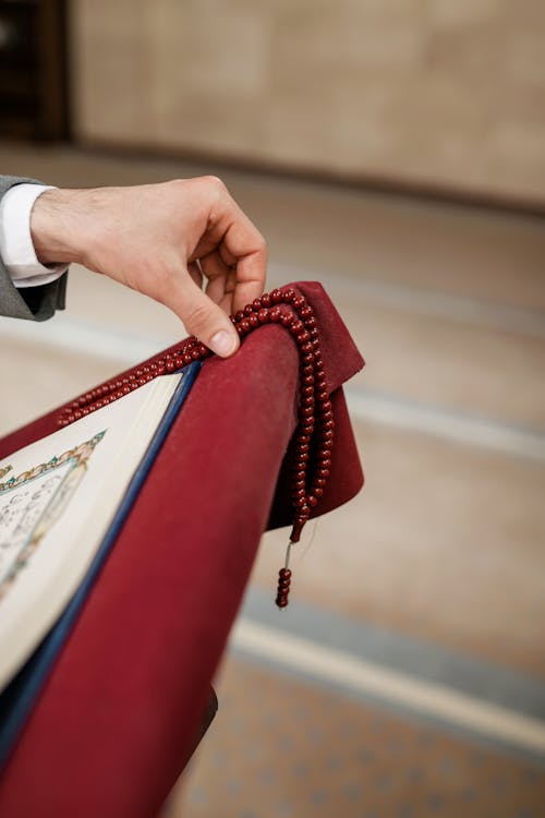 Hand Holding Praying Beads by the Corner of the Koran