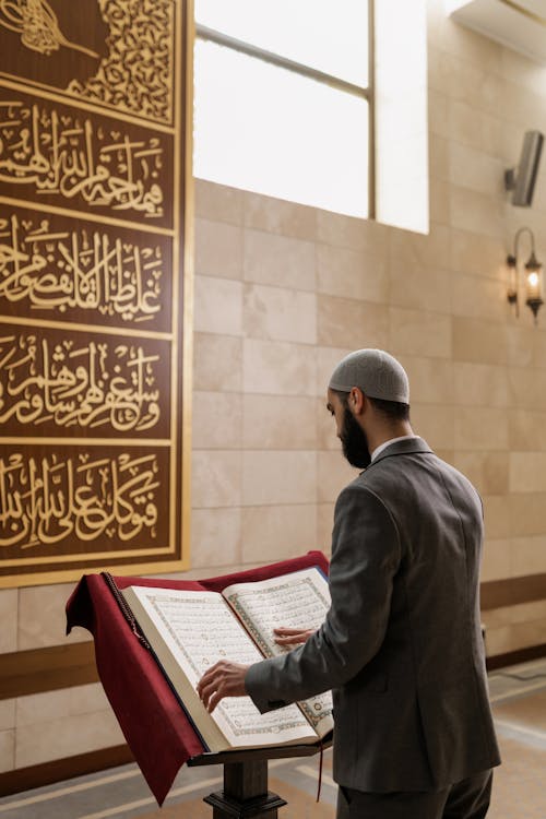 A Man in Gray Long Sleeve Suit Reading a Quran