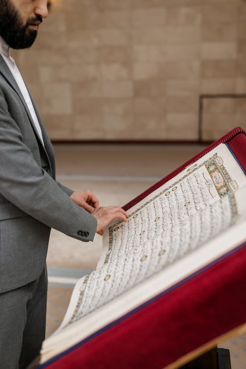 A Man in Gray Suit Reading a Koran Book