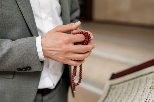 A person in formal attire holds prayer beads, reflecting Islamic culture and spirituality in a mosque setting.