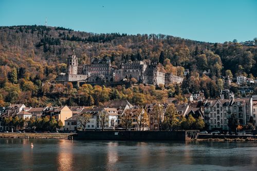Free Scenic landscape of Heidelberg Castle with lush autumn foliage and reflective river. Stock Photo