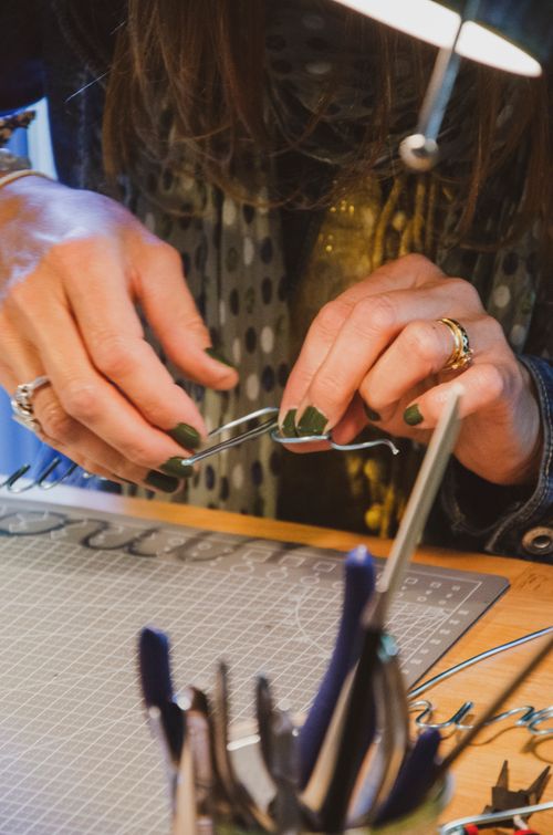 Free Close-up of hands crafting wire art in a warm workshop environment, featuring a variety of tools and materials on a desk. Stock Photo