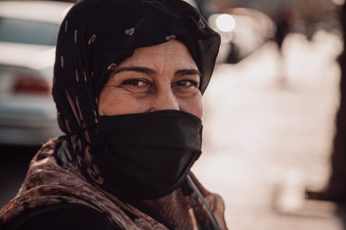 Free A mature woman wearing a headscarf and face mask is smiling outdoors. Stock Photo