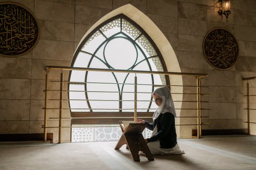 Free A woman in hijab prays and reads the Quran in a beautifully lit mosque interior. Stock Photo