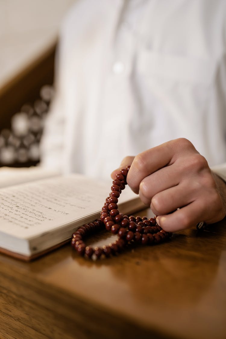 Man Hand Holding Rosary By Book