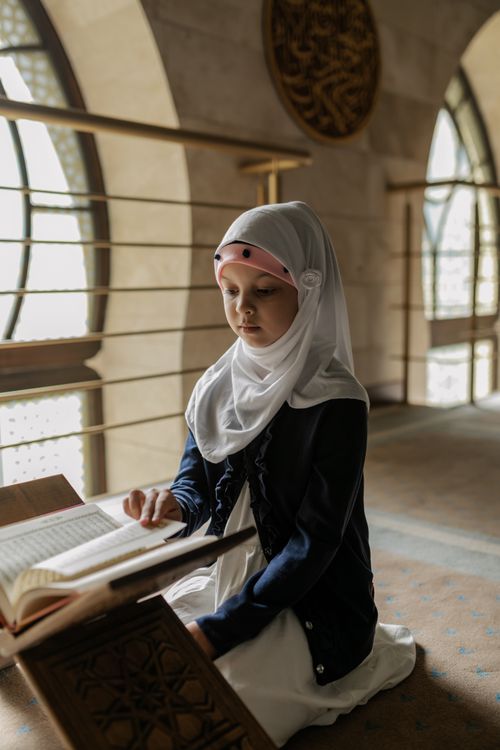 Free A young girl in a hijab reads the Quran inside a mosque, highlighting Muslim culture and spirituality. Stock Photo