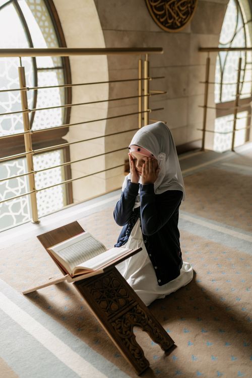 Free A young girl kneels and prays in a mosque, reading the Quran. Islamic culture and tradition. Stock Photo