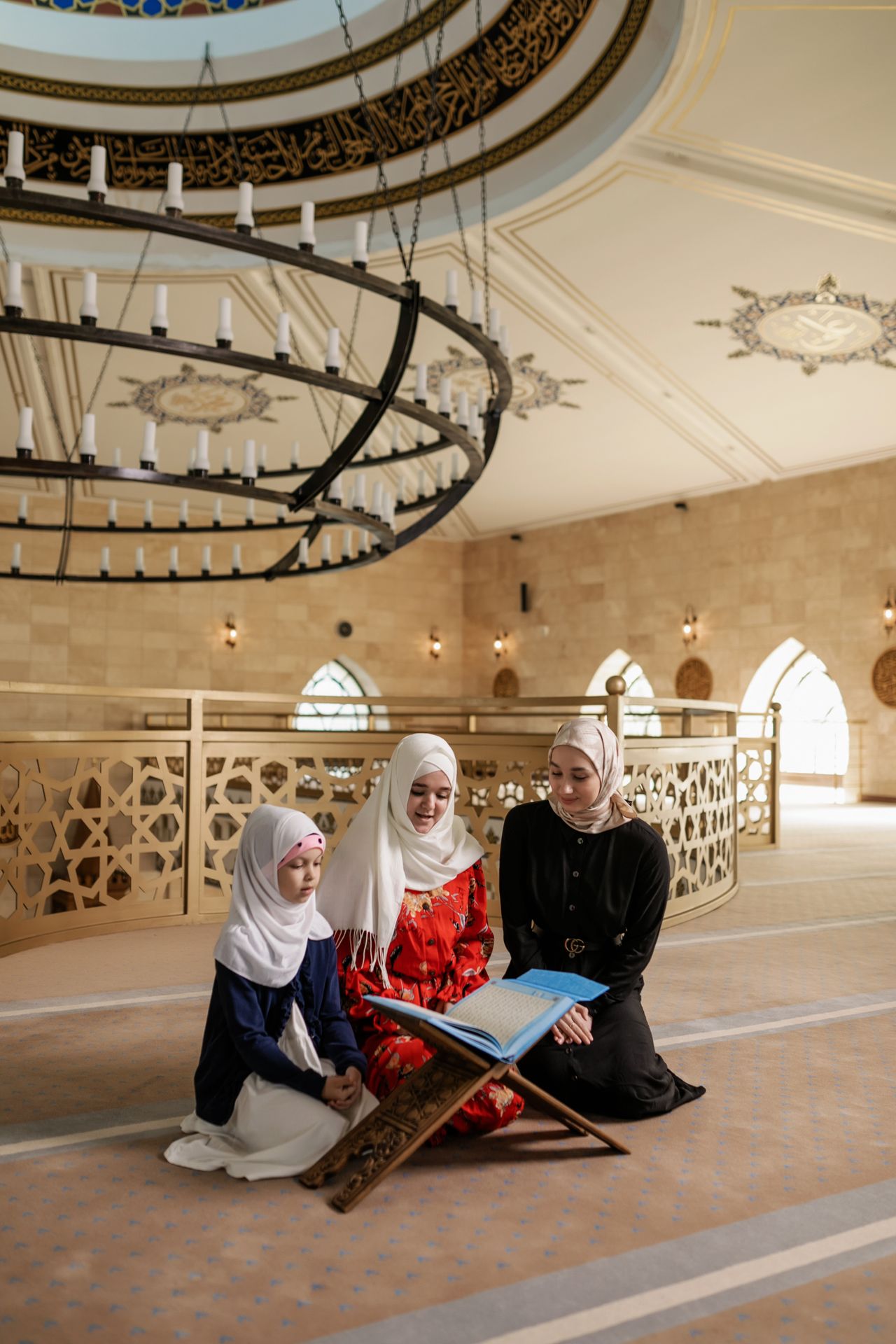 Three women in traditional attire reading inside a beautifully decorated mosque.