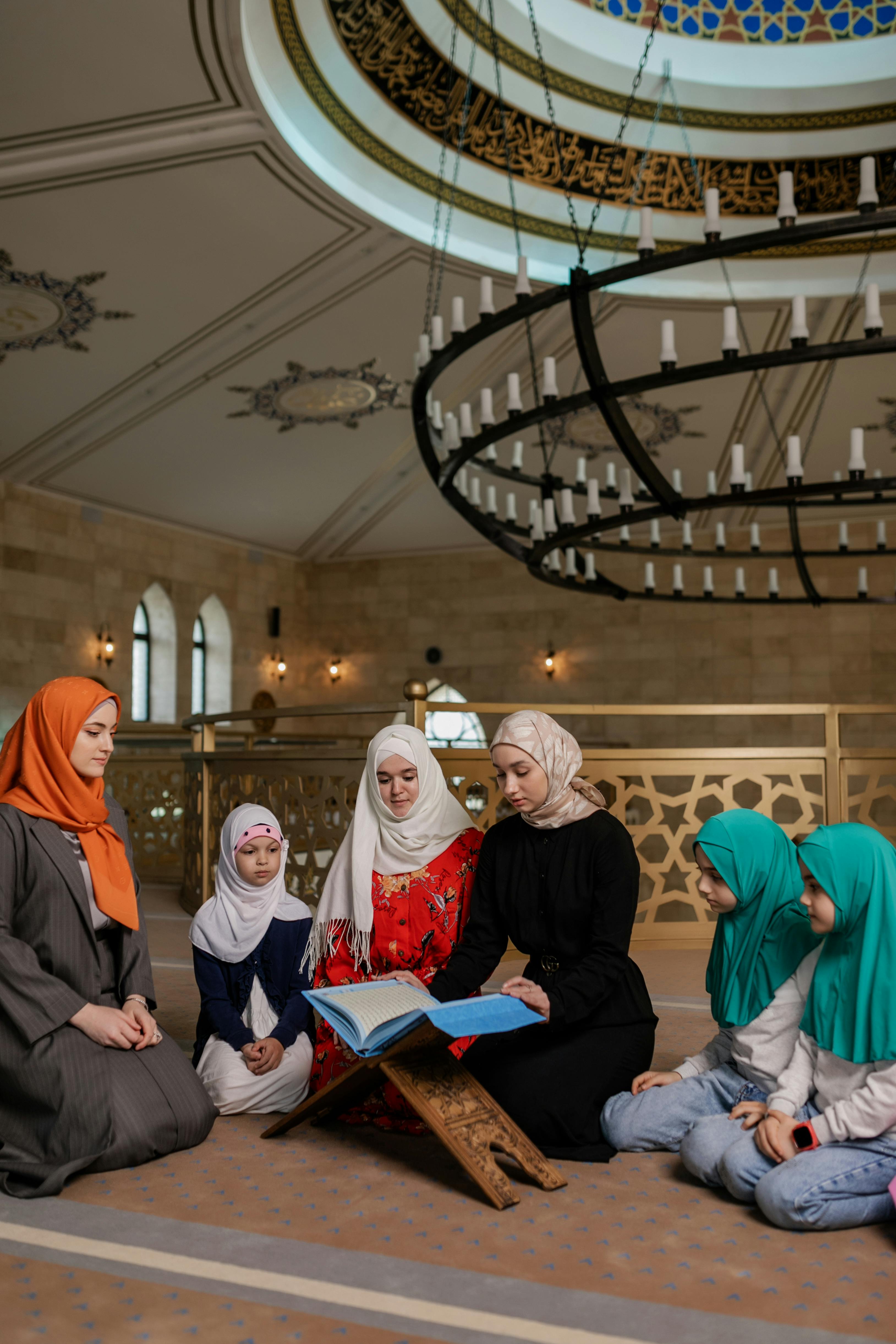 traditionally dressed women with their daughters reading the koran in a mosque