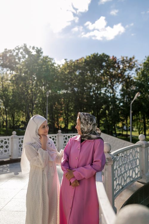 Free Two women wearing hijabs enjoy a conversation on a sunny day in a park. Stock Photo